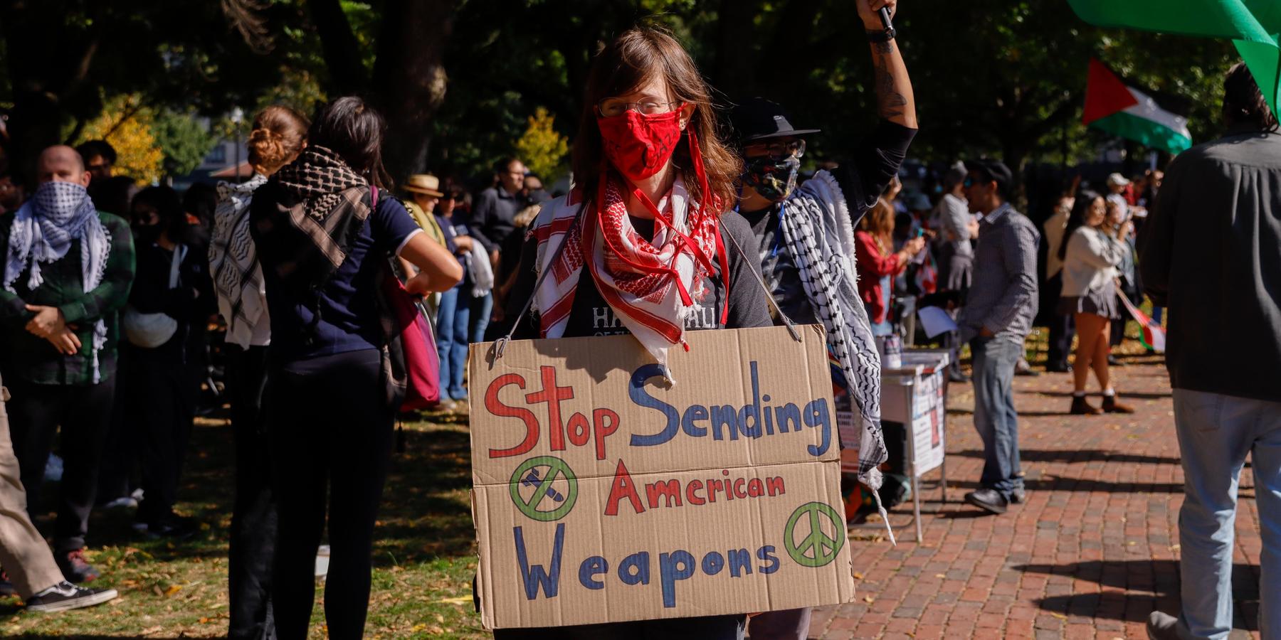 A woman participates in a protest and holds up a sign saying "stop sending American weapons"