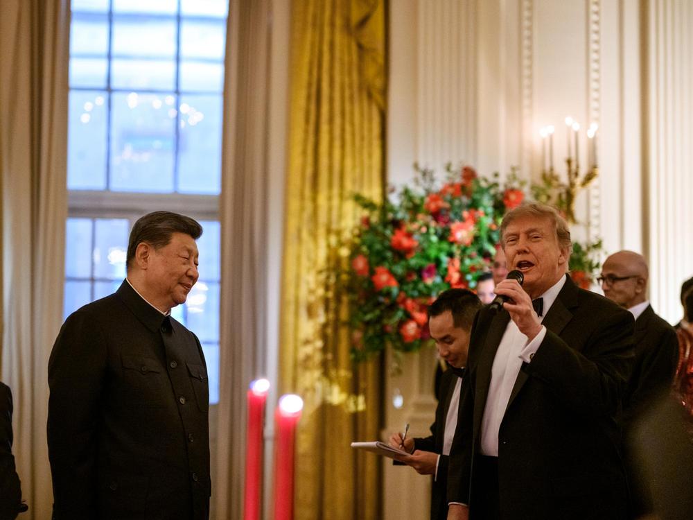 Donald Trump speaks into a microphone as Xi Jinping listens nearby