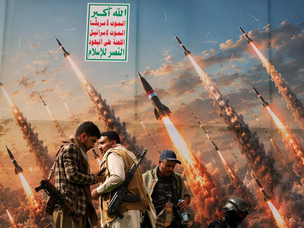 Houthi activists stand on a platform against a banner depicting Houthi missiles, at an anti-Saudi rally in Sanaa, Yemen